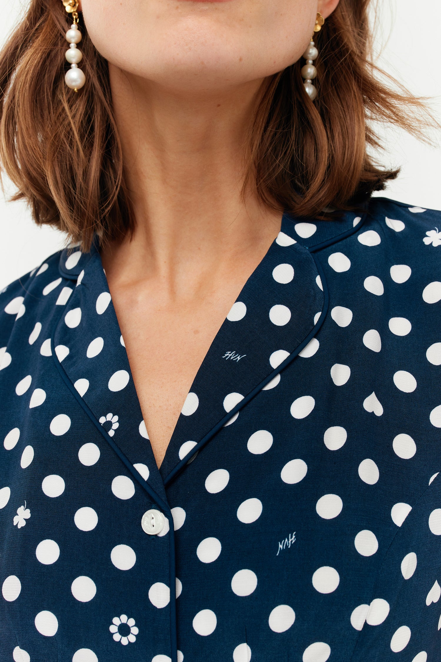 A model wears a collared shirt. The print is white polkadots on a dark navy base.