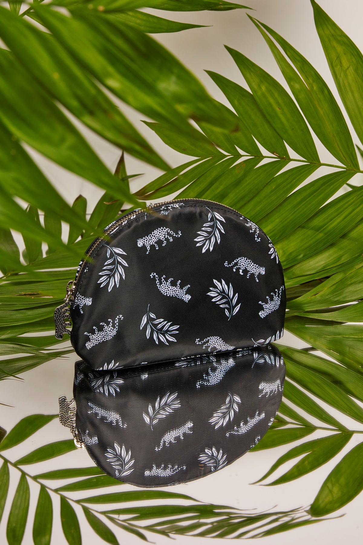 A leopard print cosmetic case with a leopard zip pull in front of palm leaves.