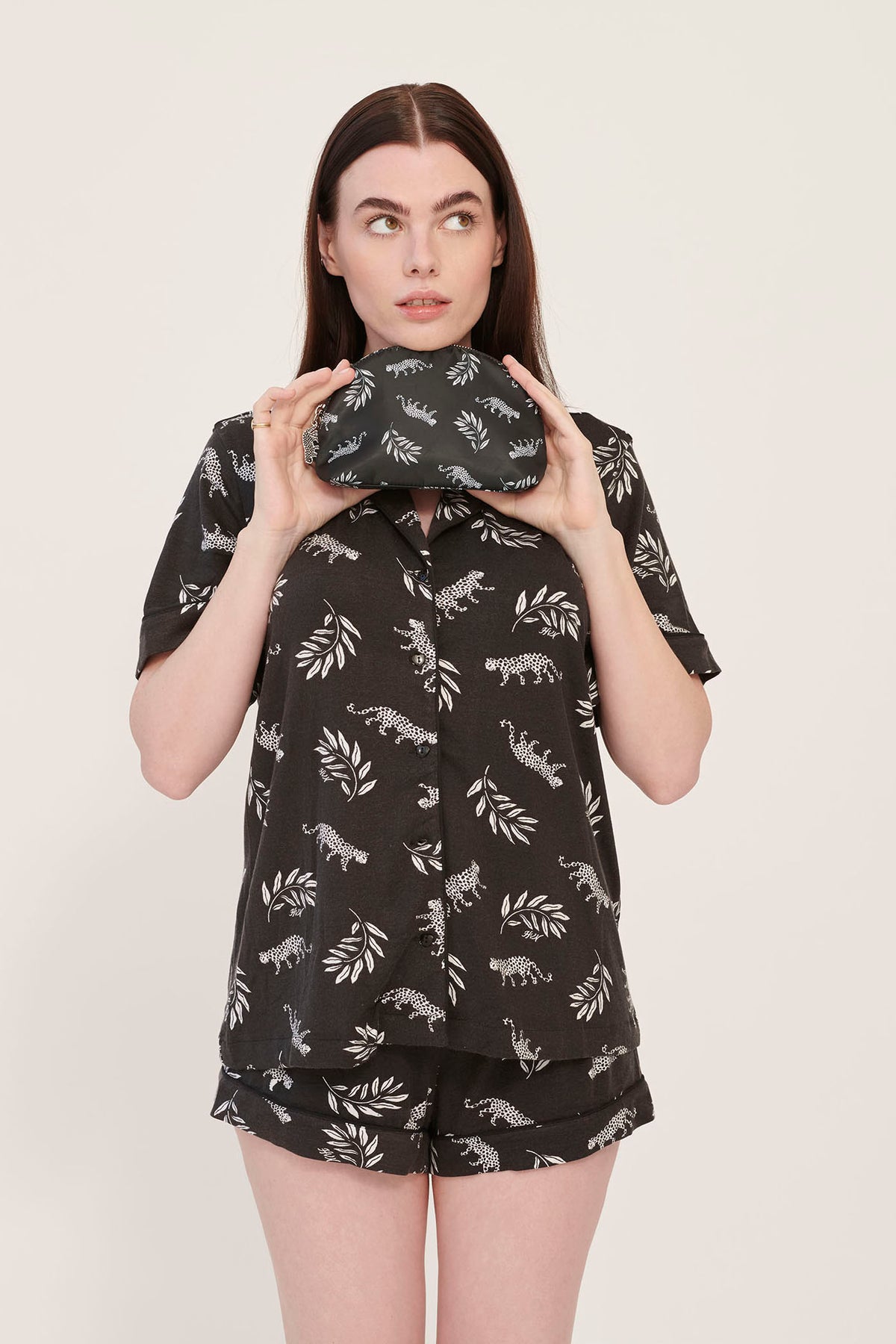 A model wearing leopard print pajamas holds a leopard print cosmetic case with a leopard zip pull.