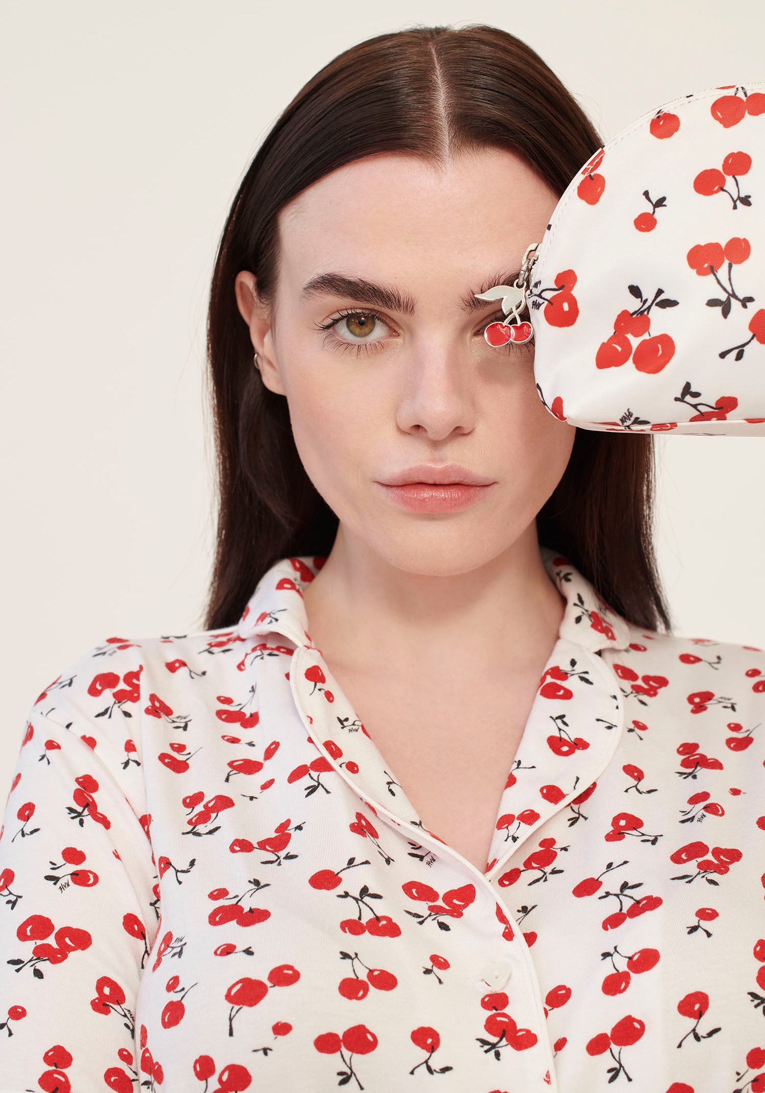 A model wearing cherry print pajamas holds a cherry print cosmetic case with a cherry zip pull.