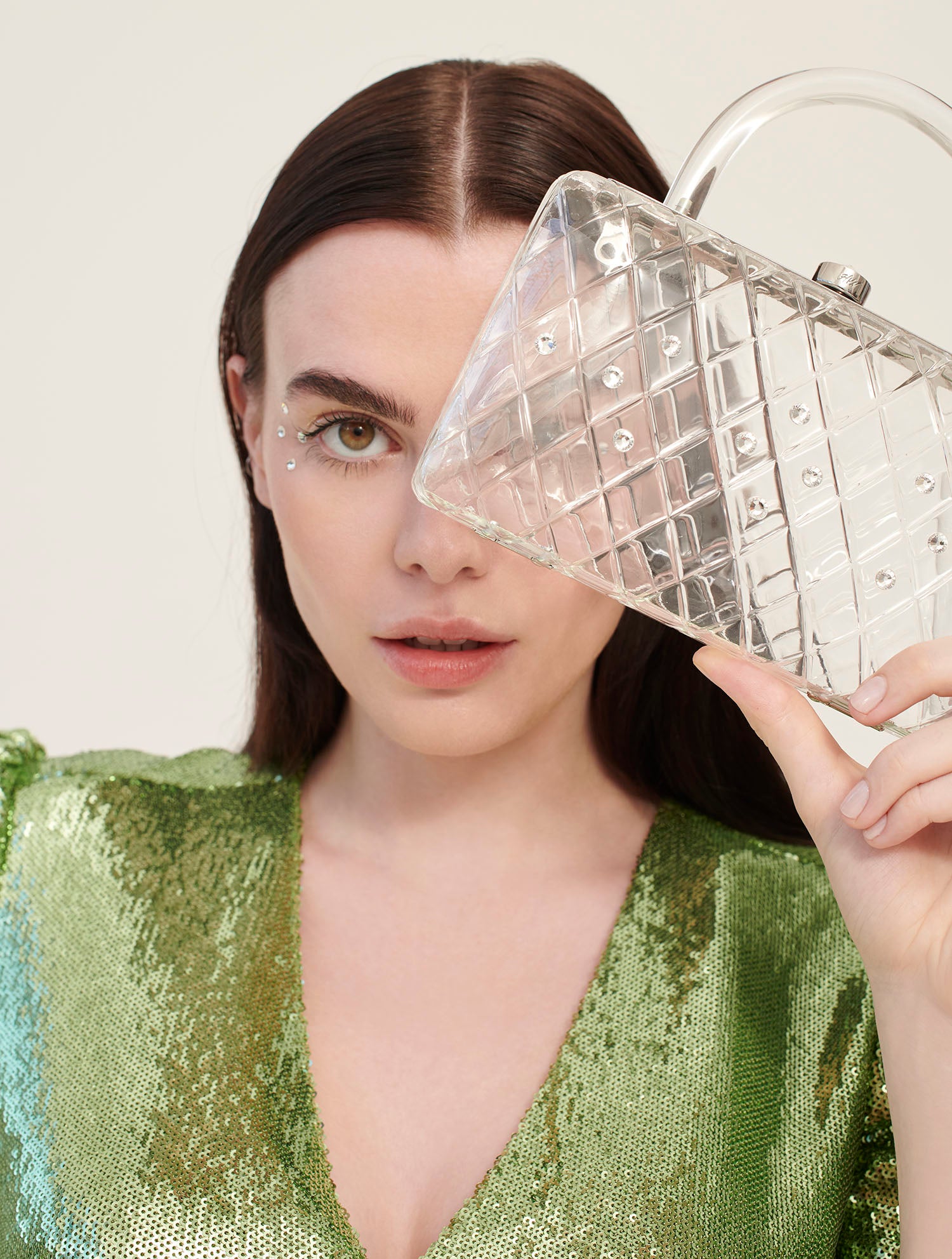 A model in a green dress holds a clear acrylic handbag with crystals and a short handle.