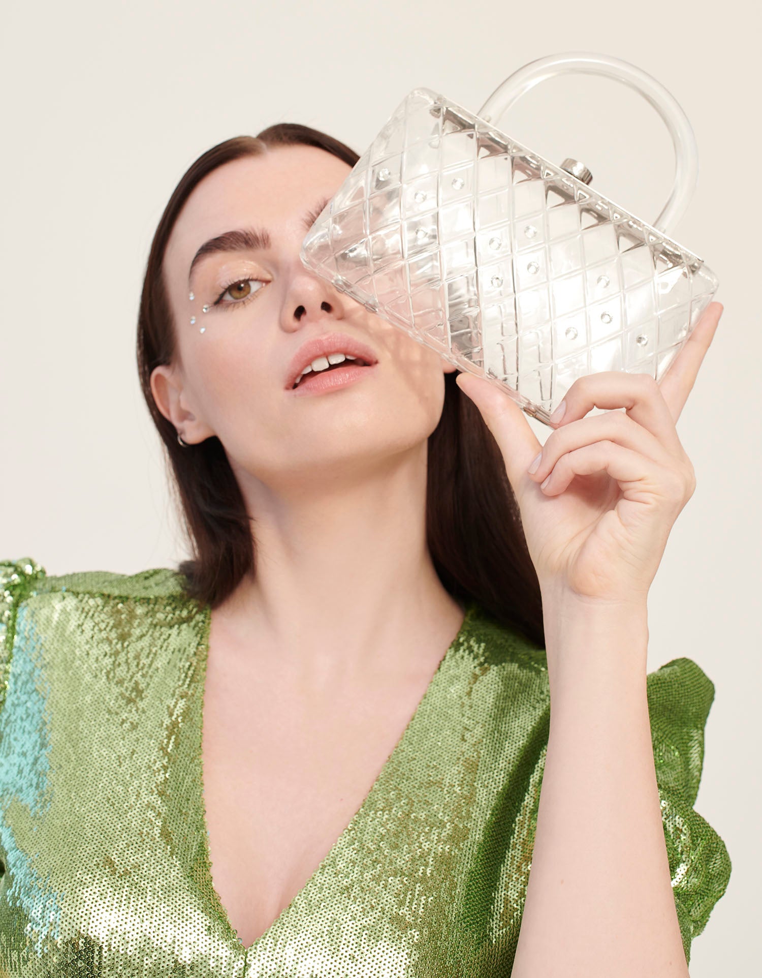 A model in a green dress holds a clear acrylic handbag with crystals and a short handle.