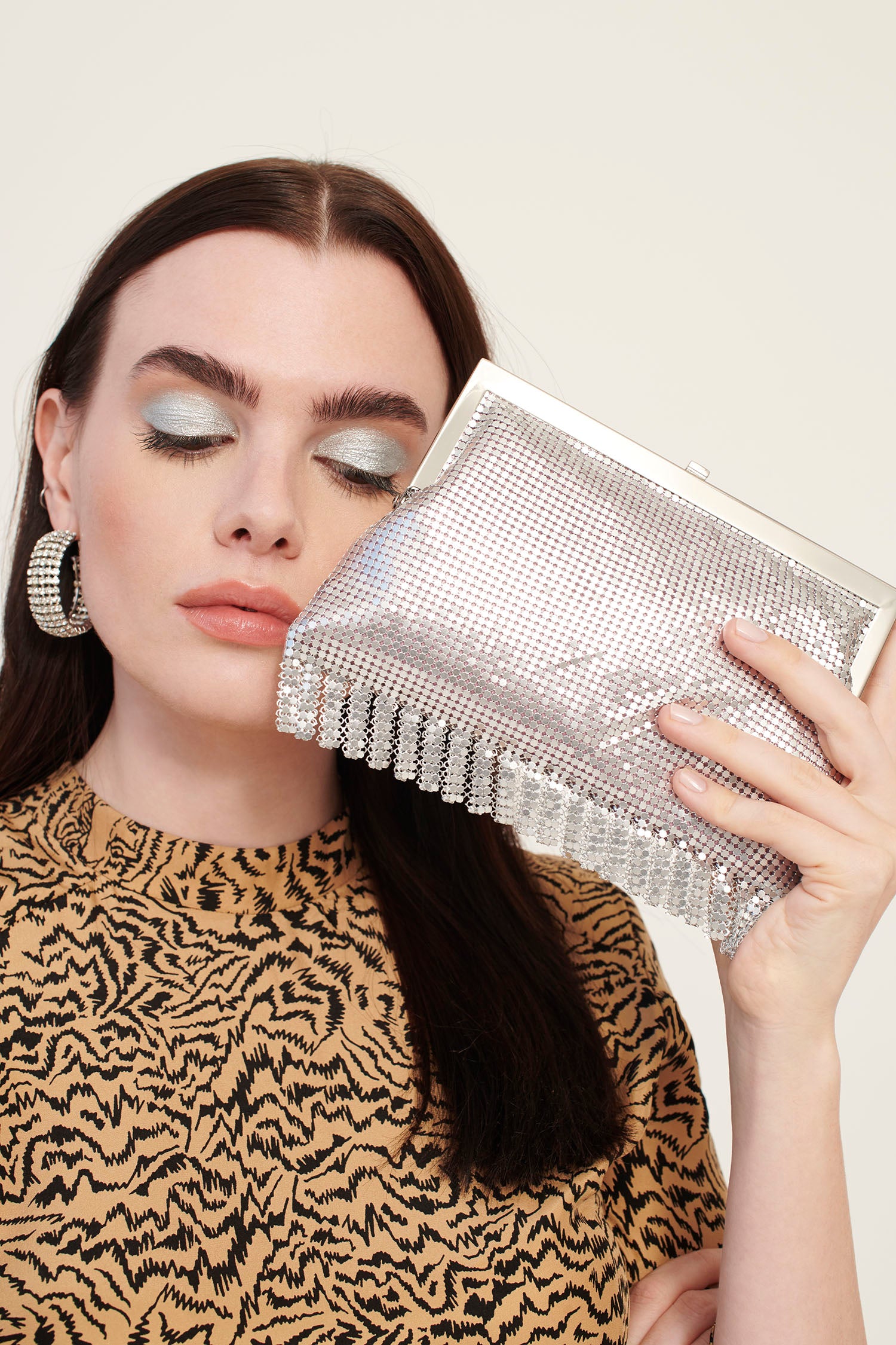A model wearing a tiger print dress holds a small, silver chainmail bag with a silver chain handle.