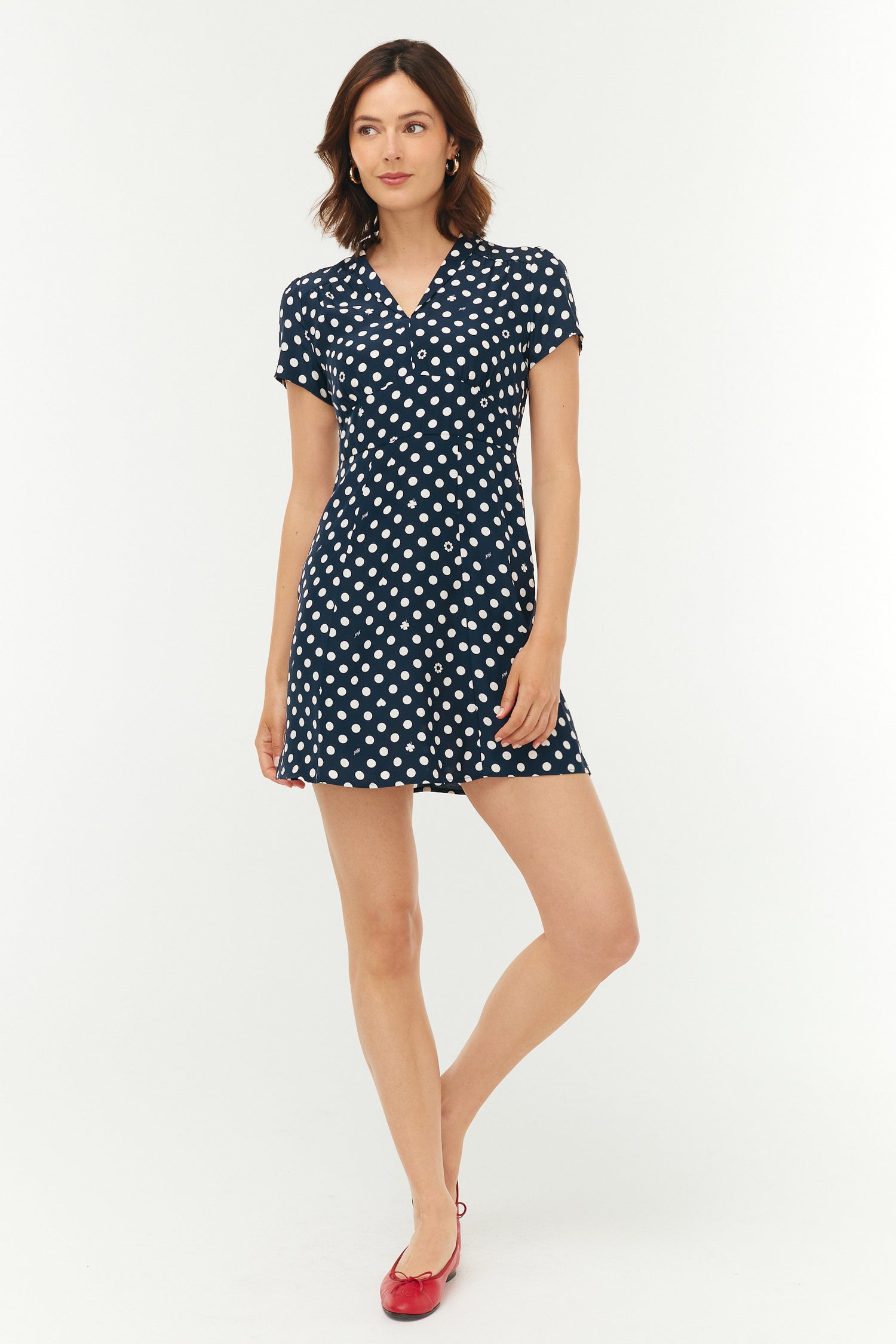 Woman wearing a navy dress with white polka dots on a white background