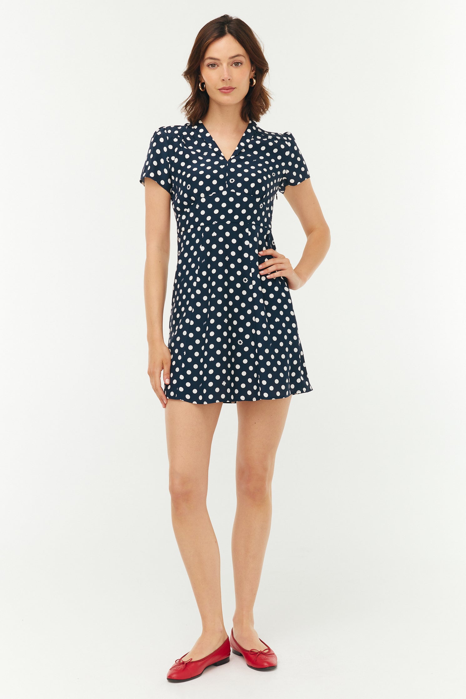 Woman wearing a navy dress with white polka dots on a white background