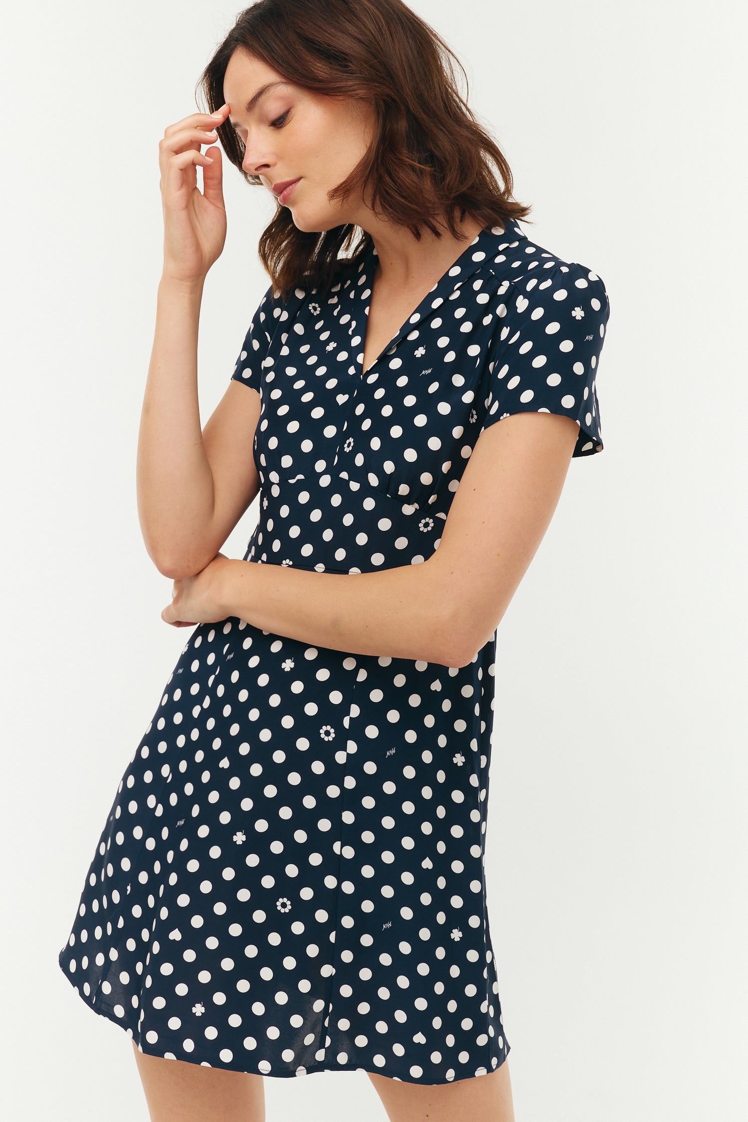 Woman wearing a navy dress with white polka dots on a plain background