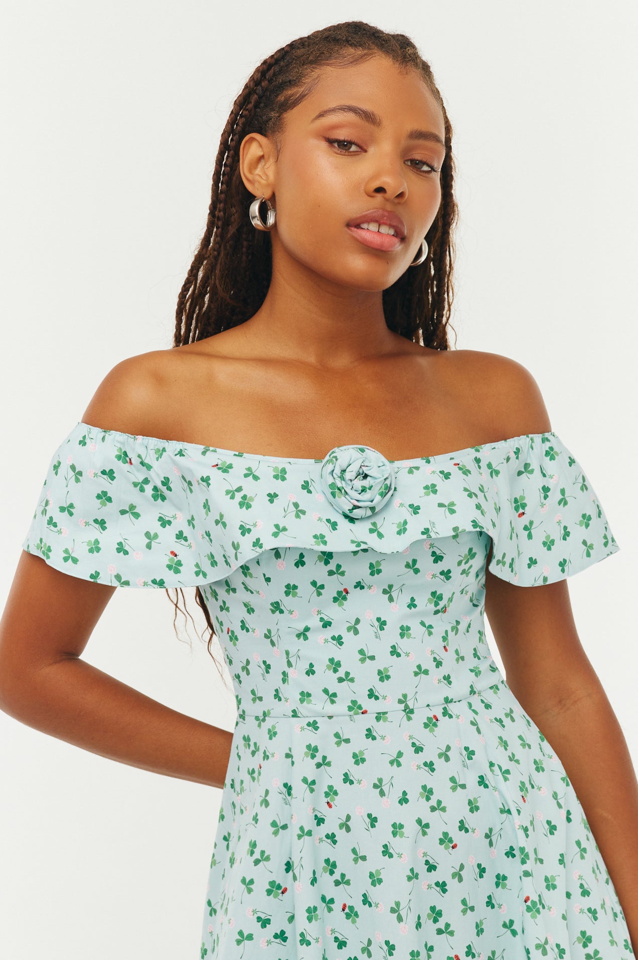 Woman wearing a light blue off-shoulder dress with green floral pattern on a white background