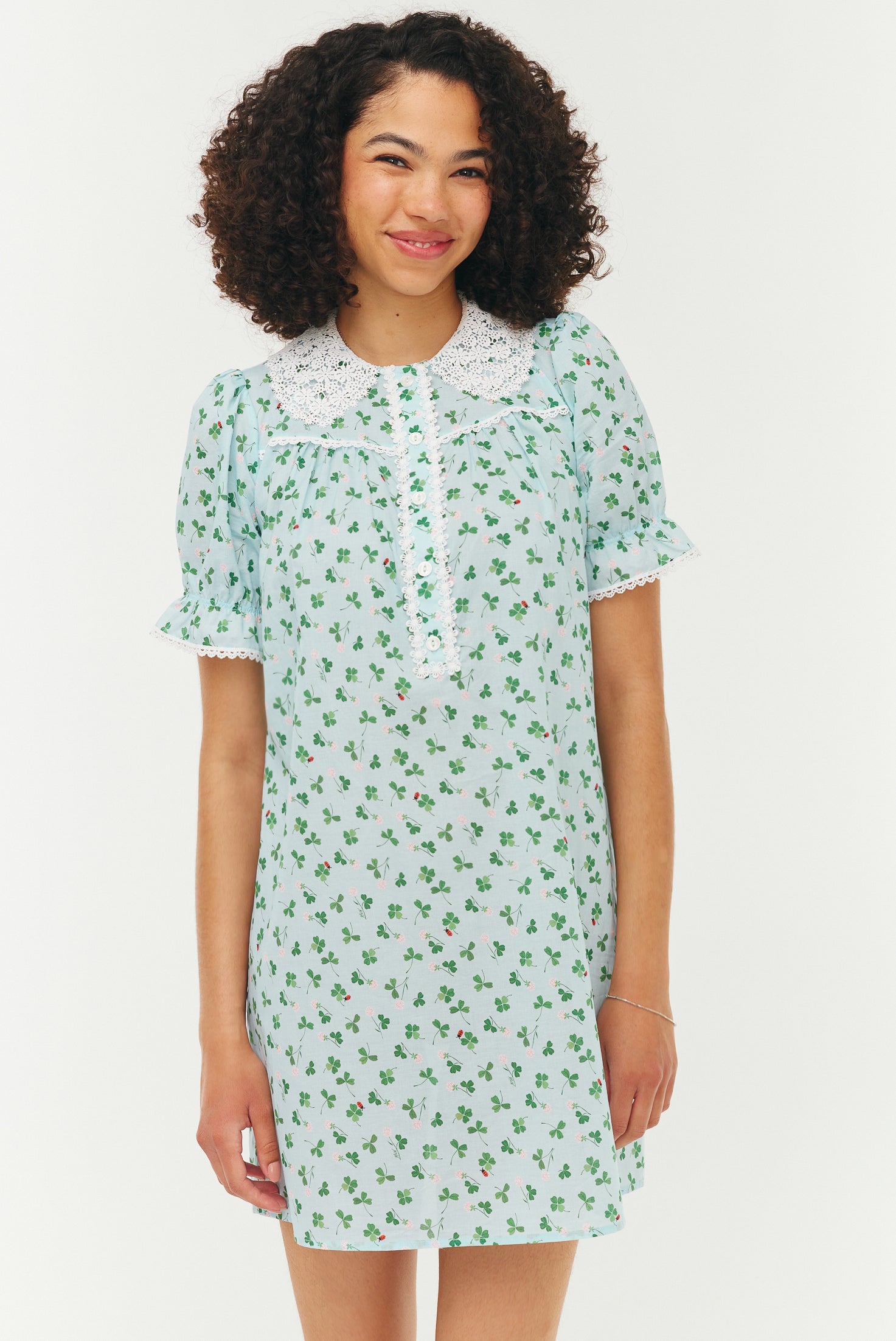 Woman wearing a light green floral dress with a white collar on a white background