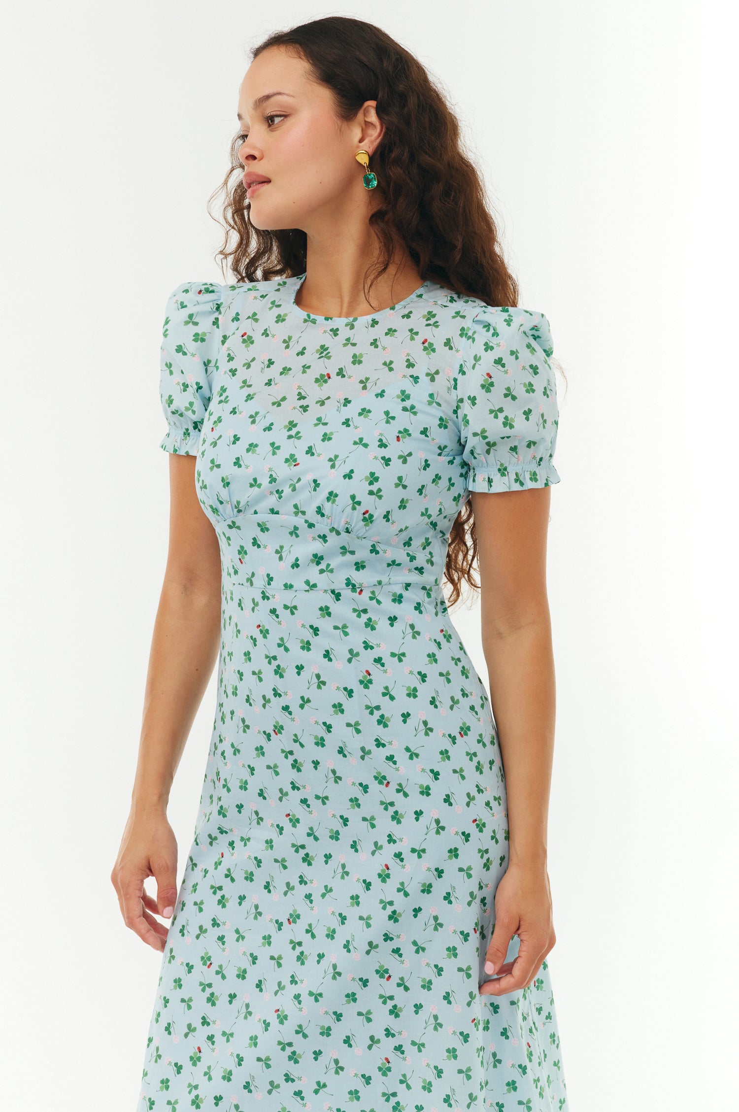 Woman wearing a light blue dress with green floral pattern on a white background