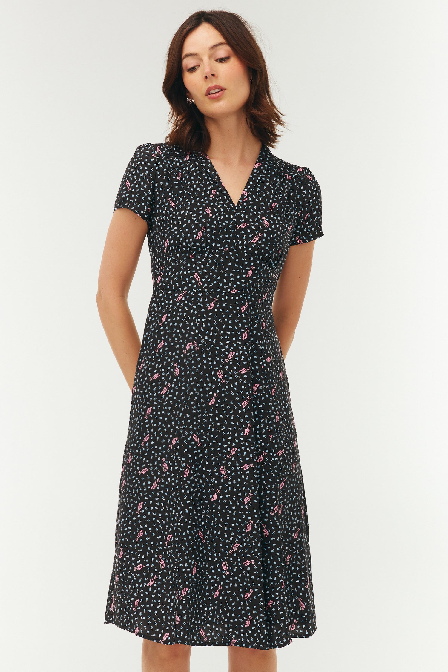 Woman wearing a black dress with pink ballet slippers and a blue floral pattern on a white background. 