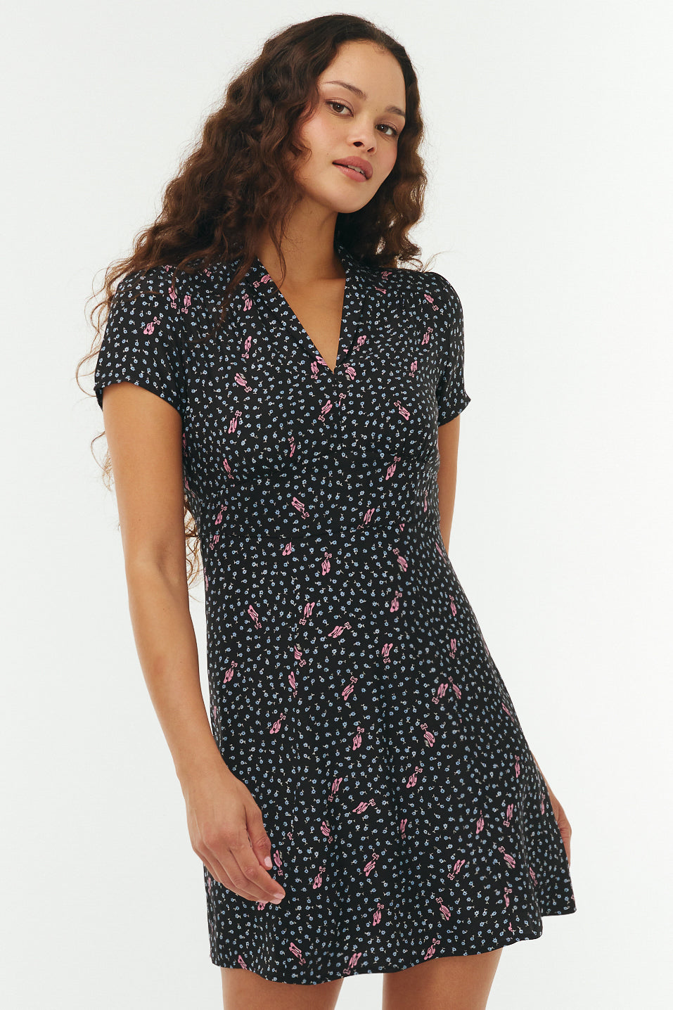 Woman wearing a black floral mini dress with pink ballet slippers on a white background