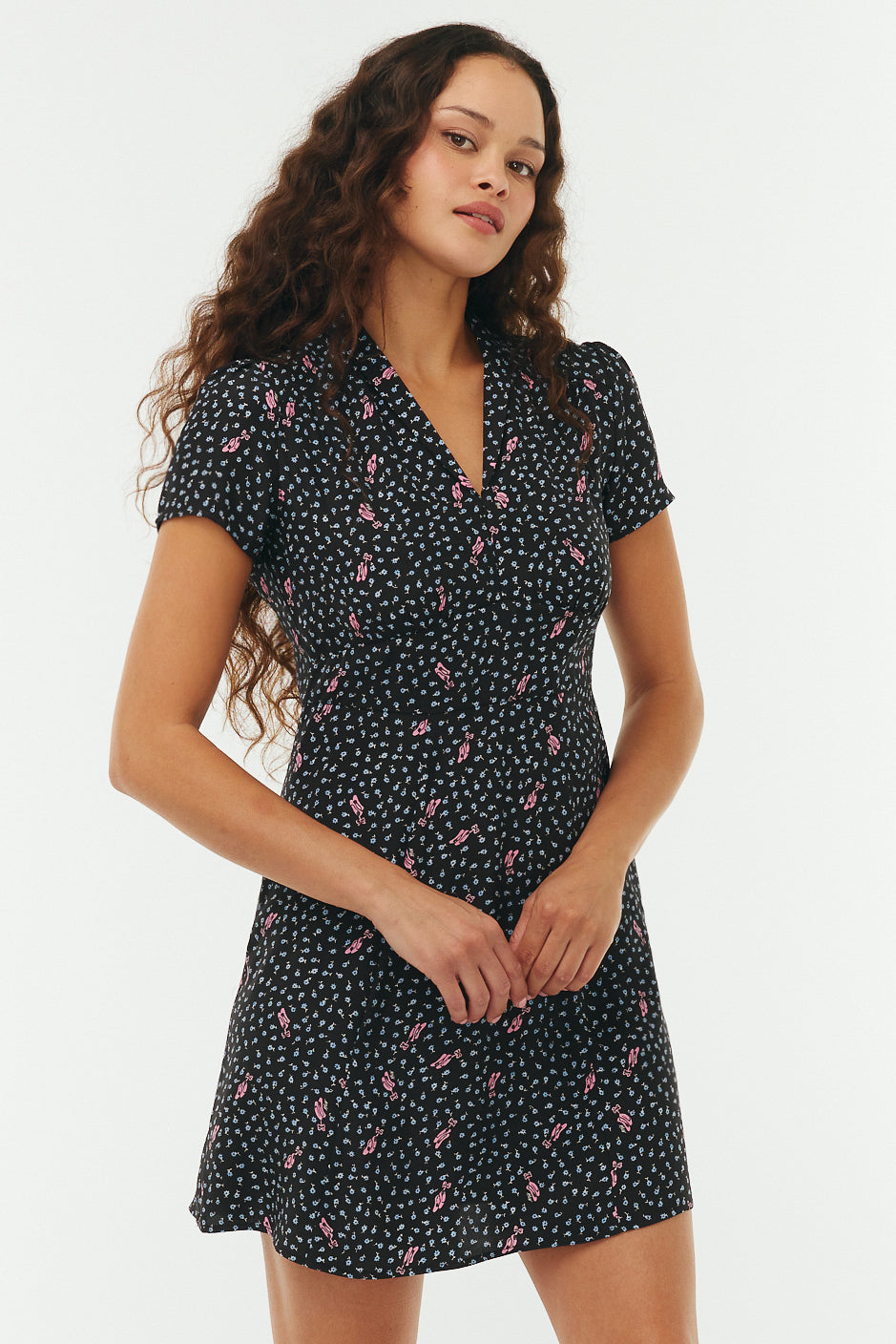Woman wearing a black floral mini dress with pink ballet slippers on a white background. 
