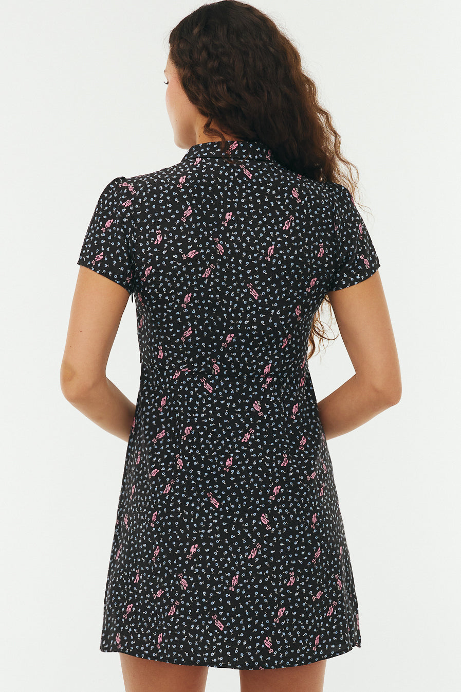 Woman from the back wearing a black floral mini dress with pink ballet slippers on a white background. 