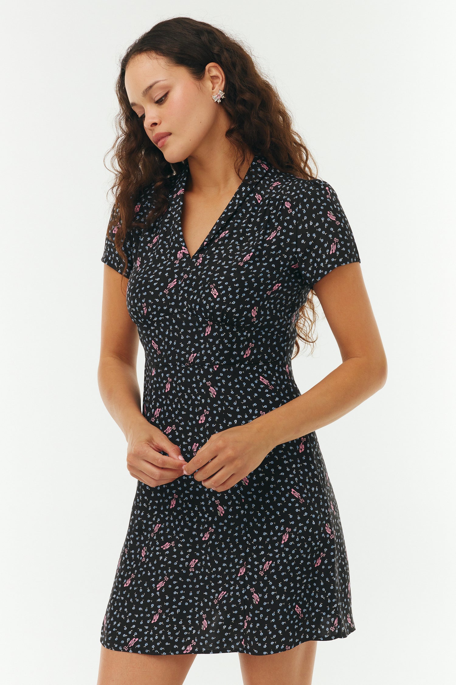 Woman wearing a black floral mini dress with pink ballet slippers on a white background. 