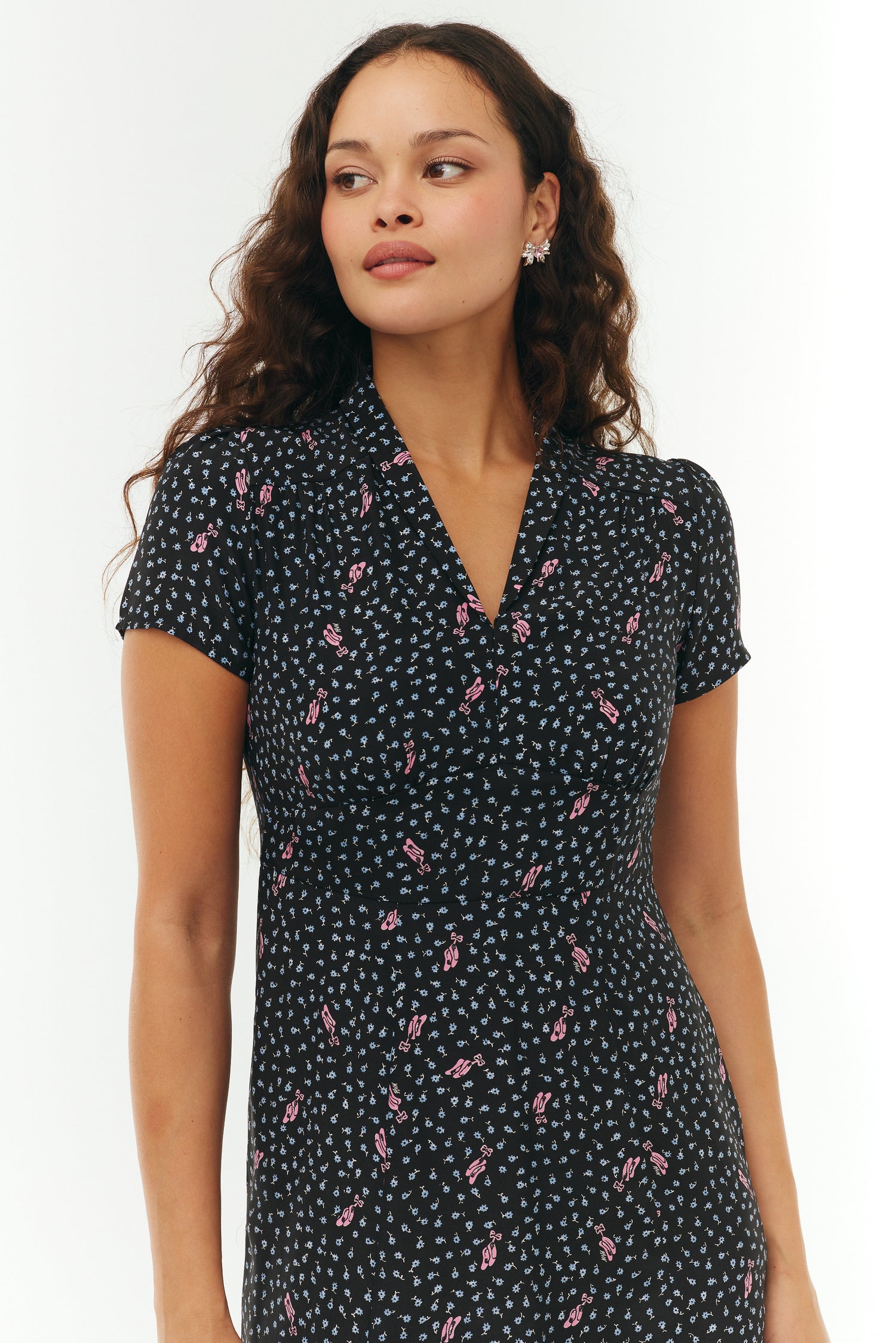 Woman wearing a black floral mini dress with pink ballet slippers on a white background. 