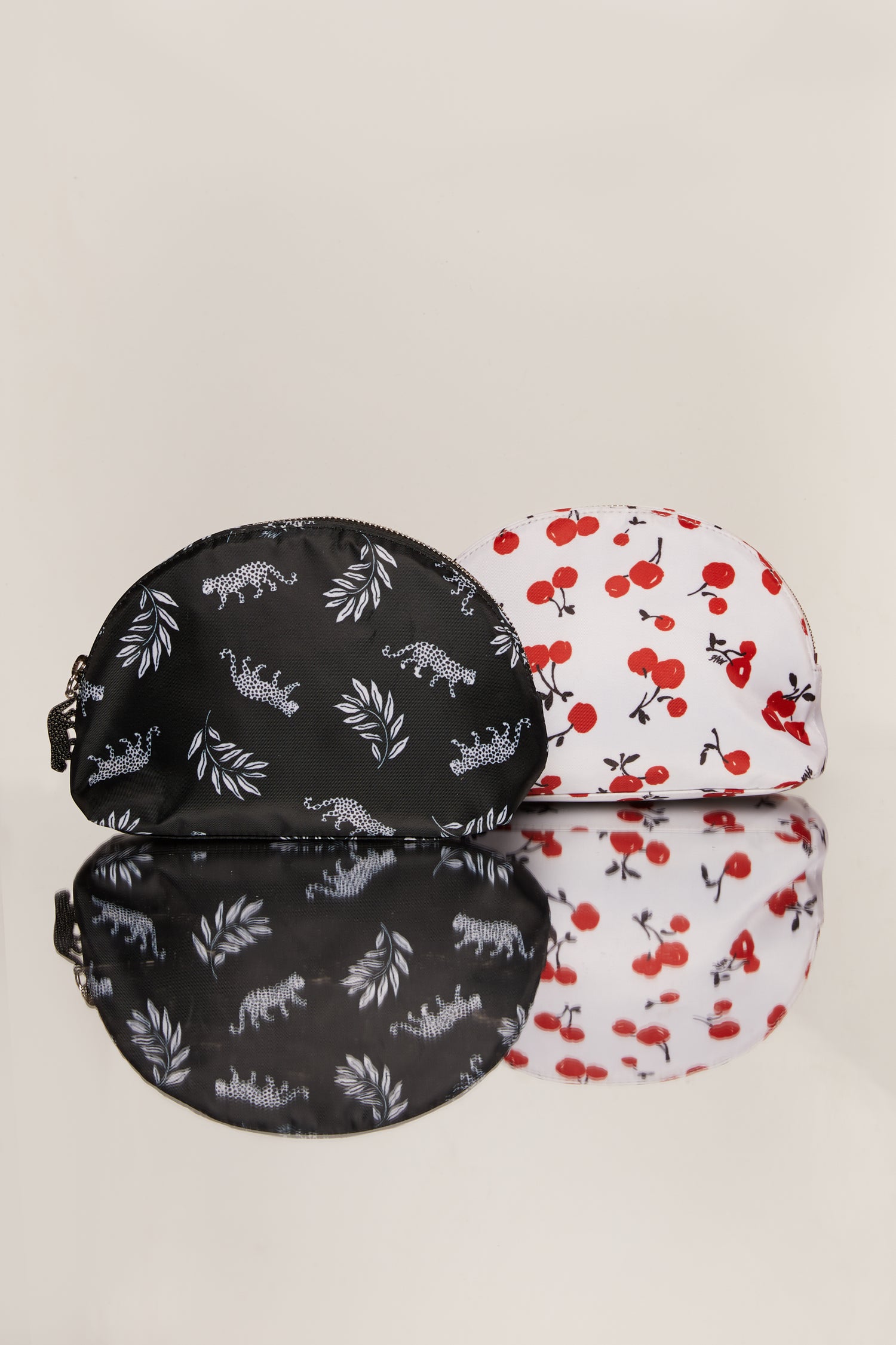 A cherry print cosmetic case with a cherry zip pull next to a leopard print cosmetic case with a leopard zip pull.