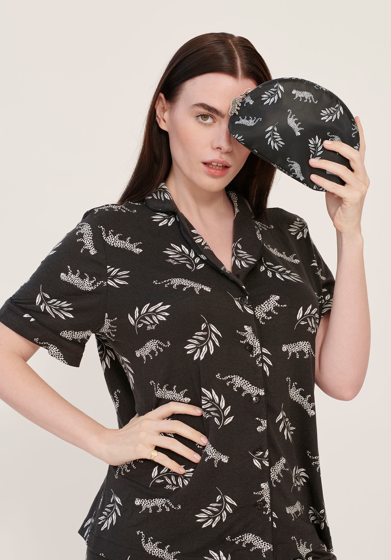 A model wearing leopard print pajamas holds a leopard print cosmetic case with a leopard zip pull.