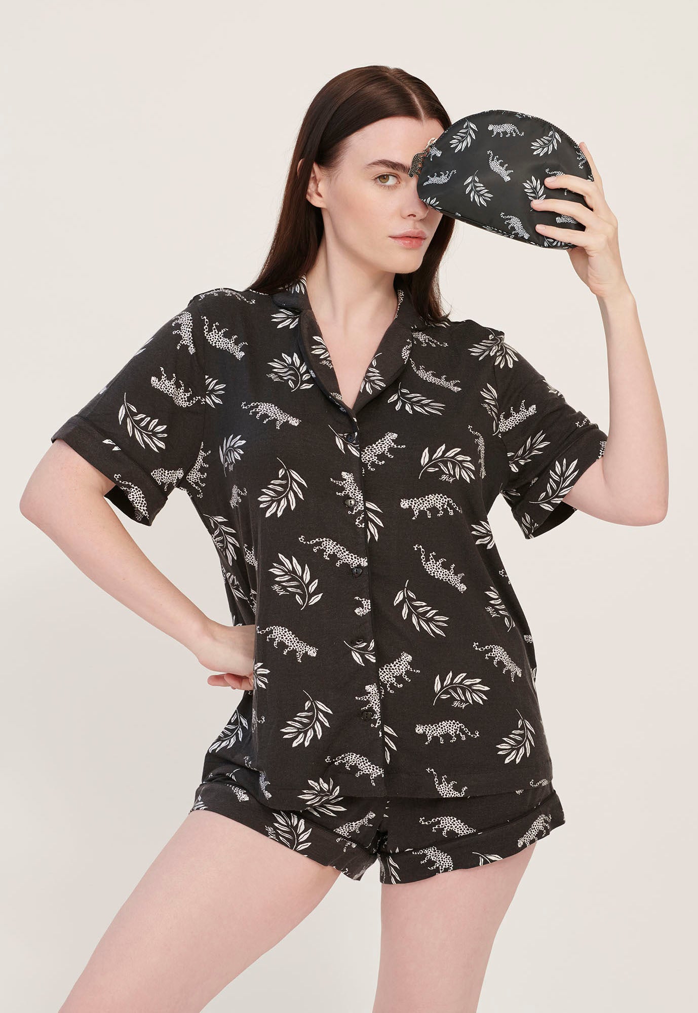 A model wearing leopard print pajamas holds a leopard print cosmetic case with a leopard zip pull.