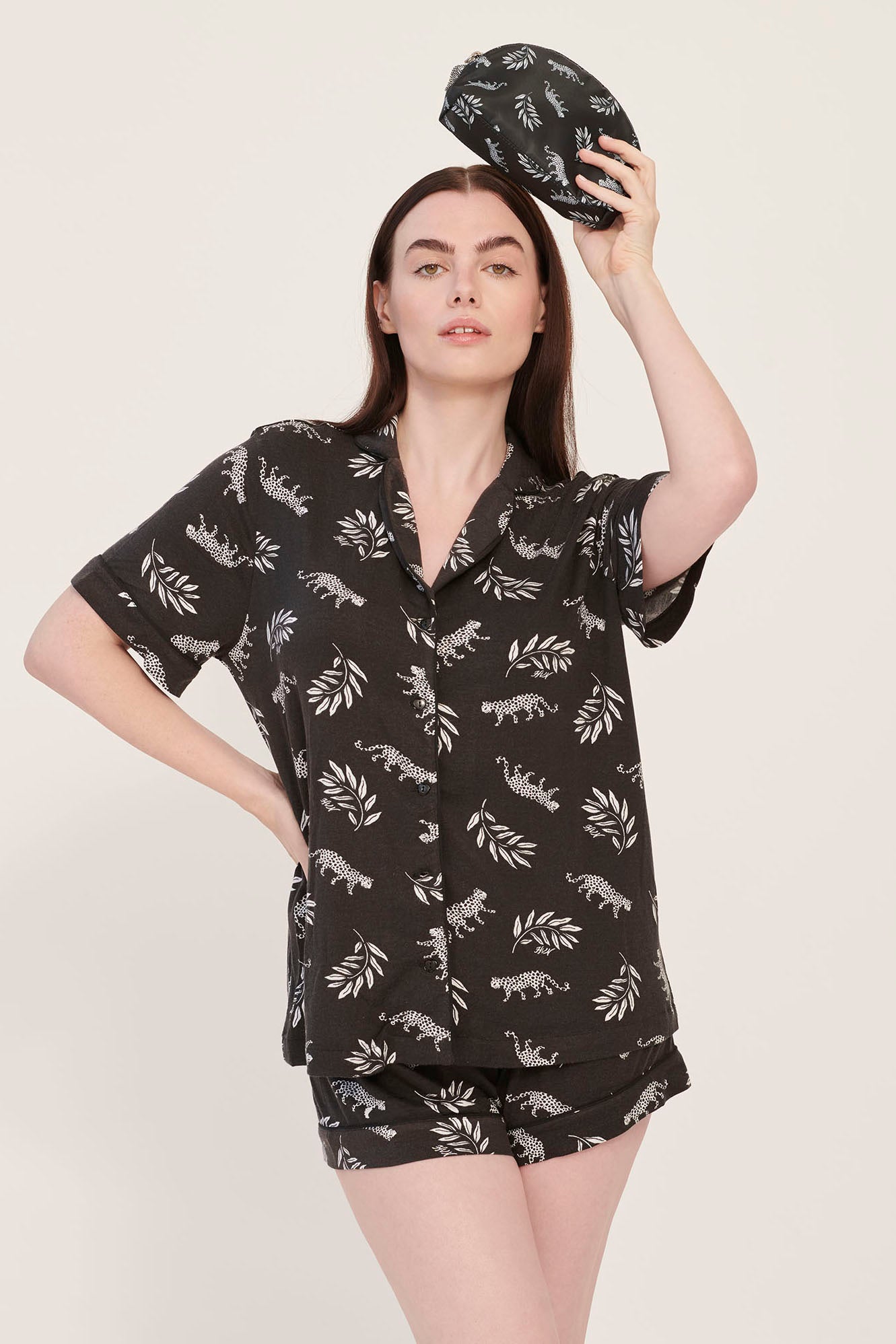 A model wearing leopard print pajamas holds a leopard print cosmetic case with a leopard zip pull.