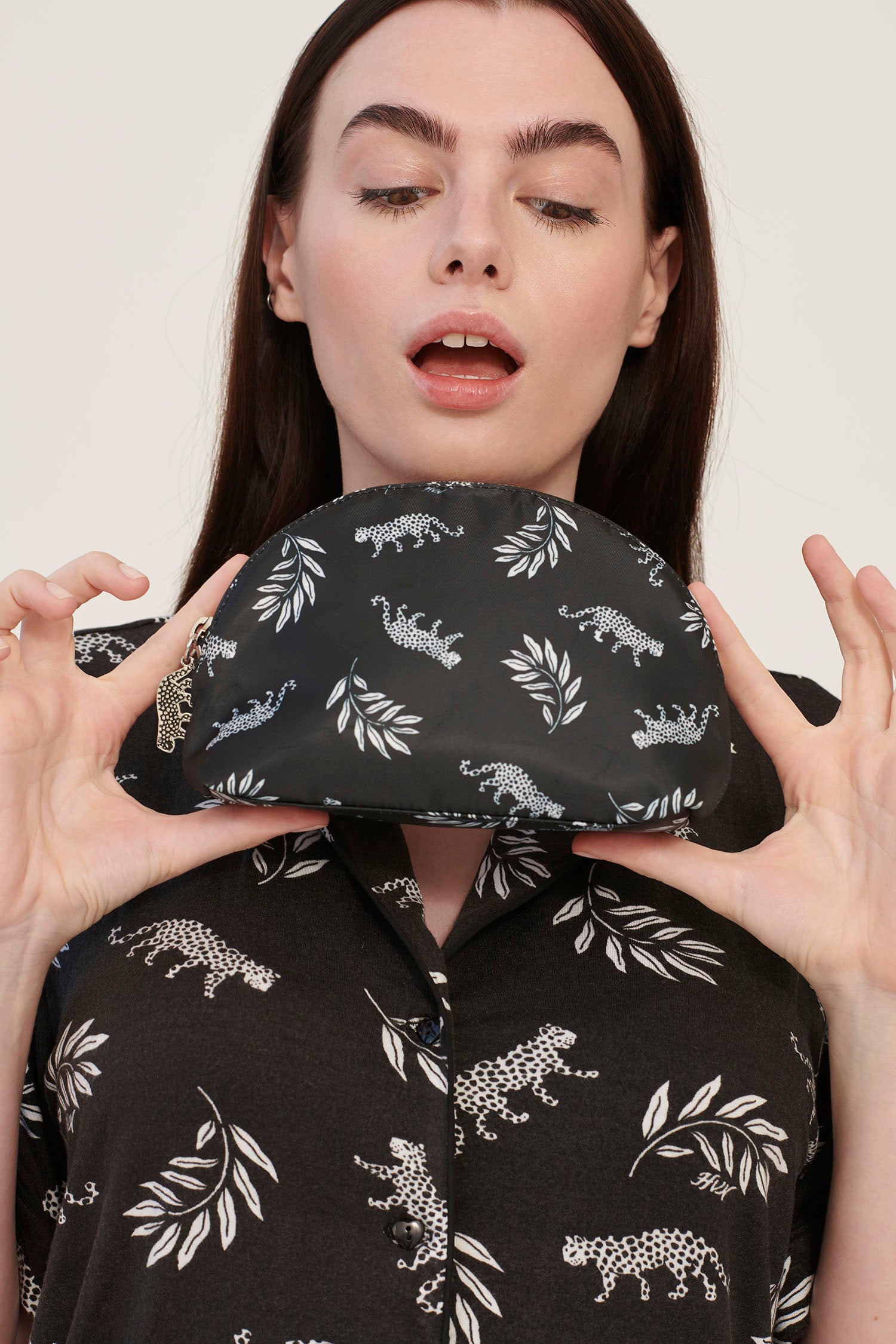 A model wearing leopard print pajamas holds a leopard print cosmetic case with a leopard zip pull.