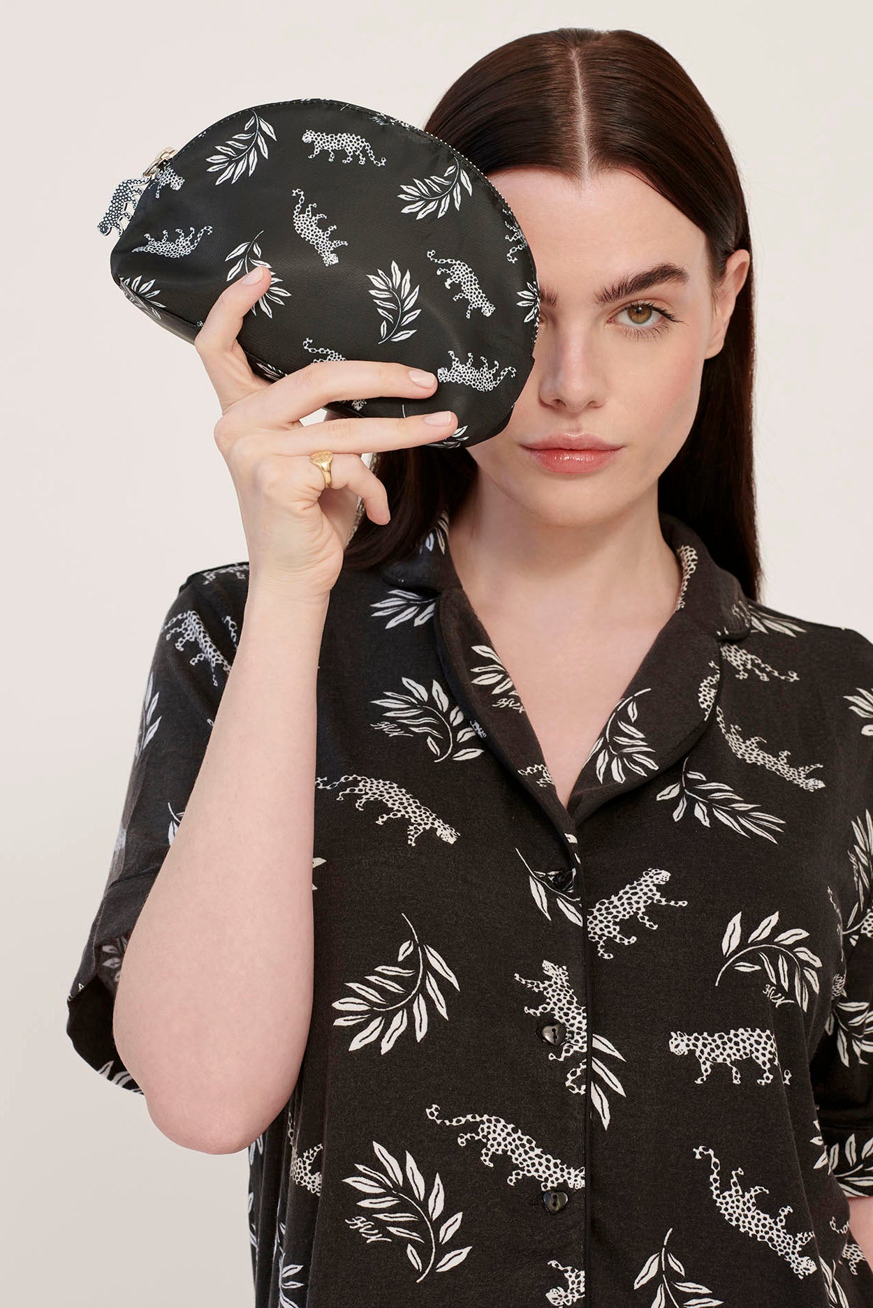 A model wearing leopard print pajamas holds a leopard print cosmetic case with a leopard zip pull.