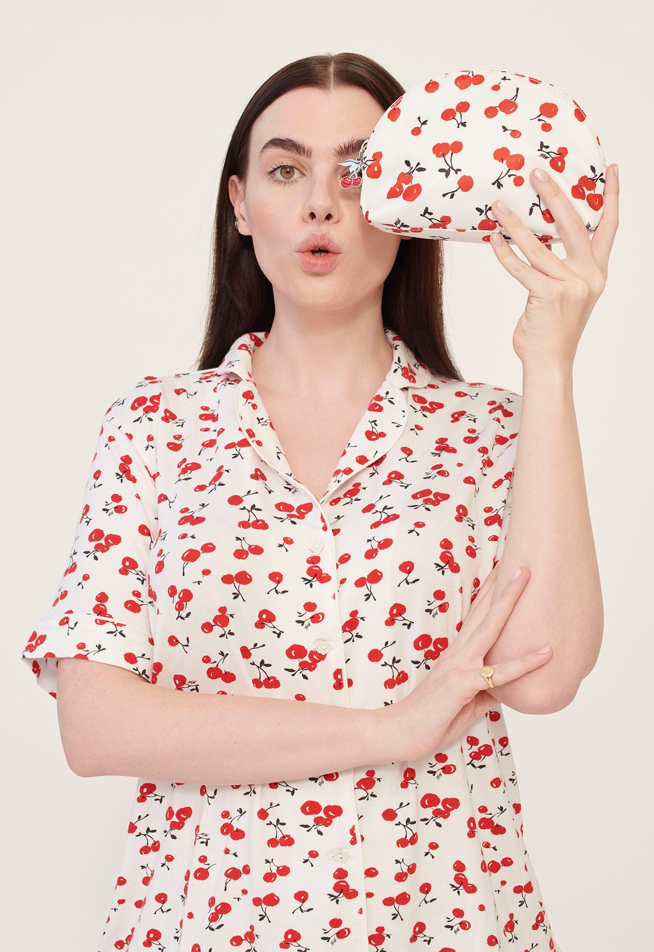 A model wearing cherry print pajamas holds a cherry print cosmetic case with a cherry zip pull. 
