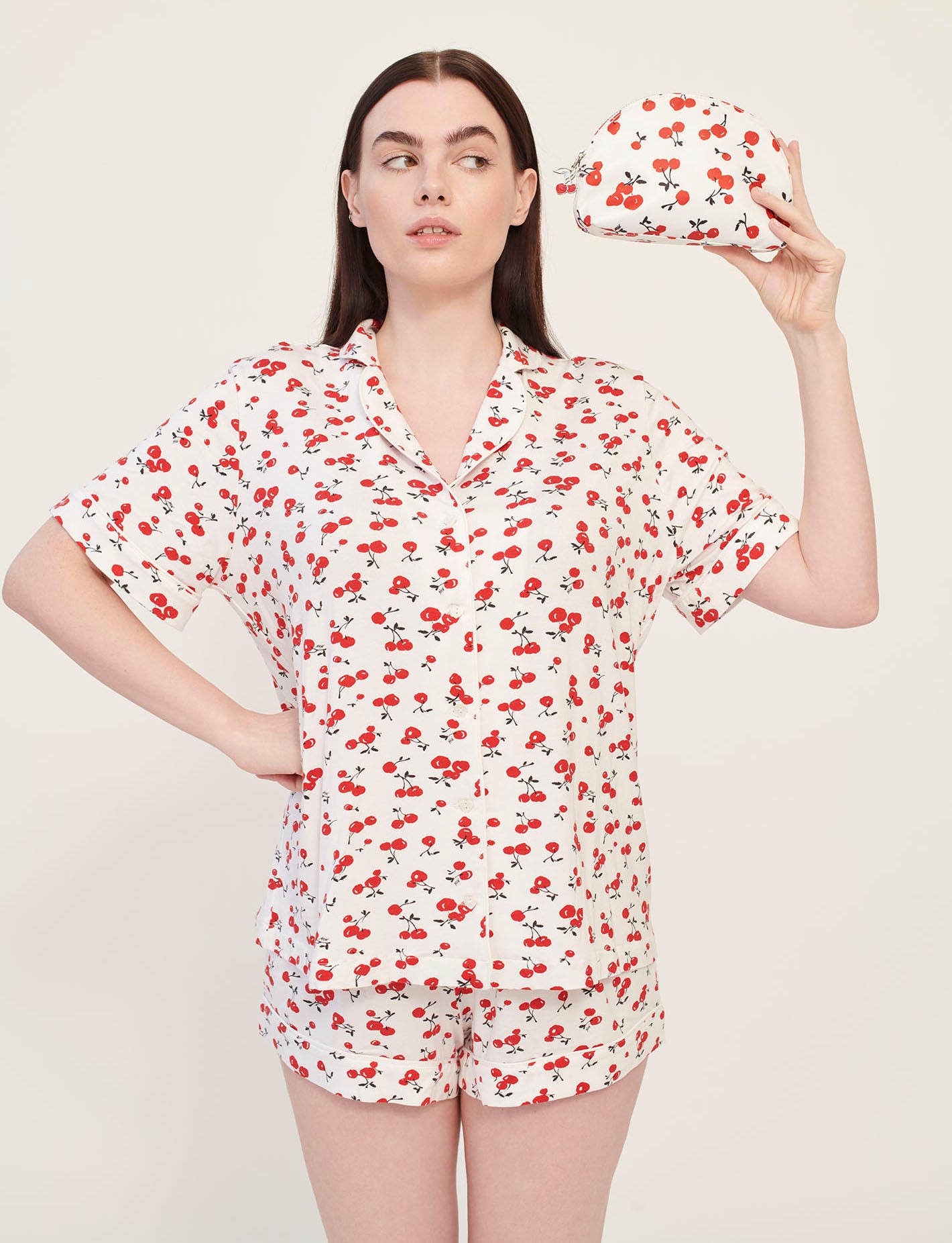 A model wearing cherry print pajamas holds a cherry print cosmetic case with a cherry zip pull. 