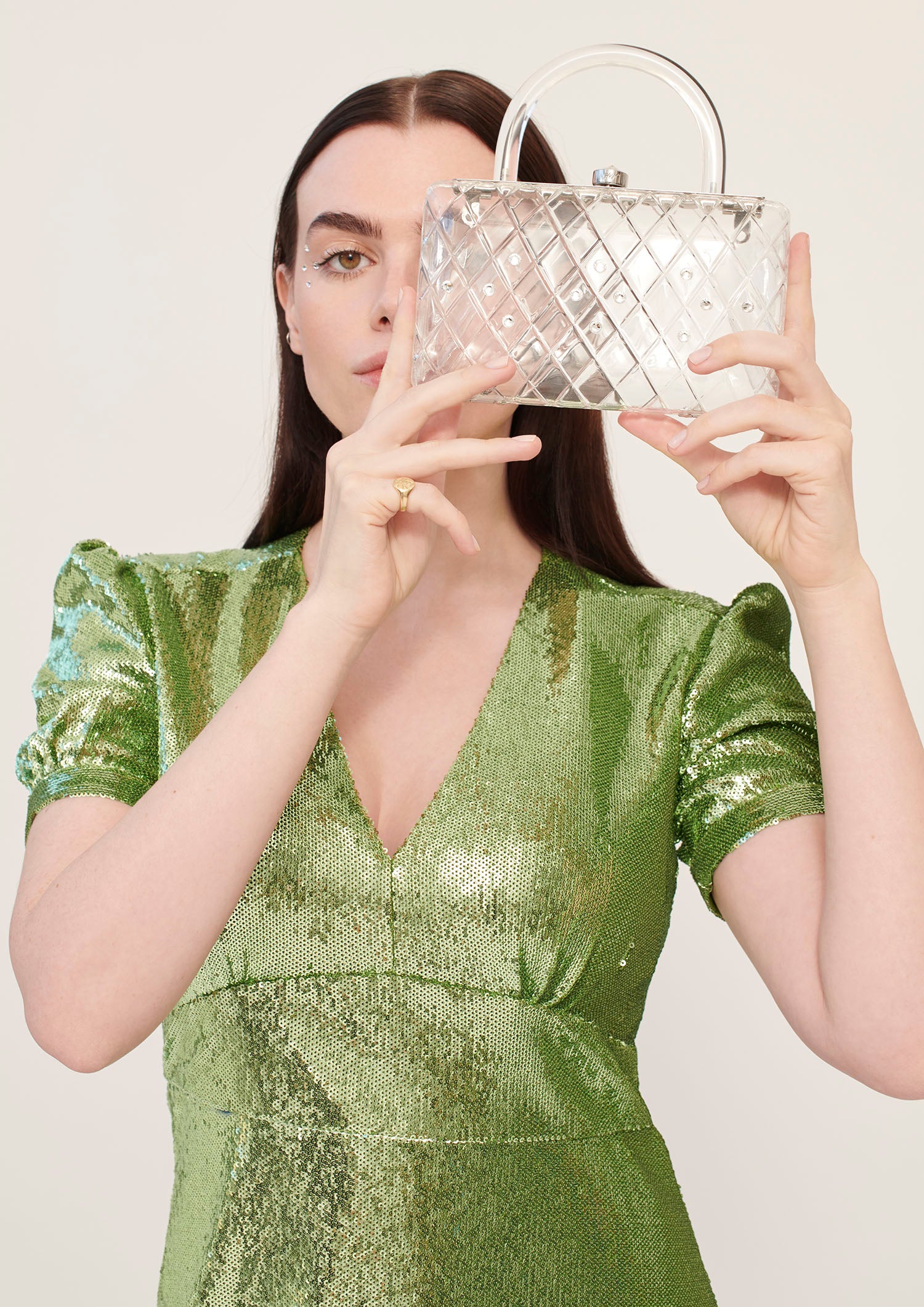 A model in a green dress holds a clear acrylic handbag with crystals and a short handle. 