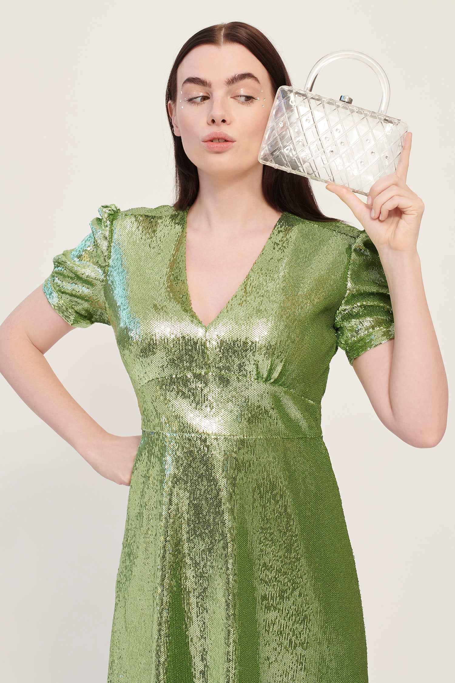 A model in a green dress holds a clear acrylic handbag with crystals and a short handle. 
