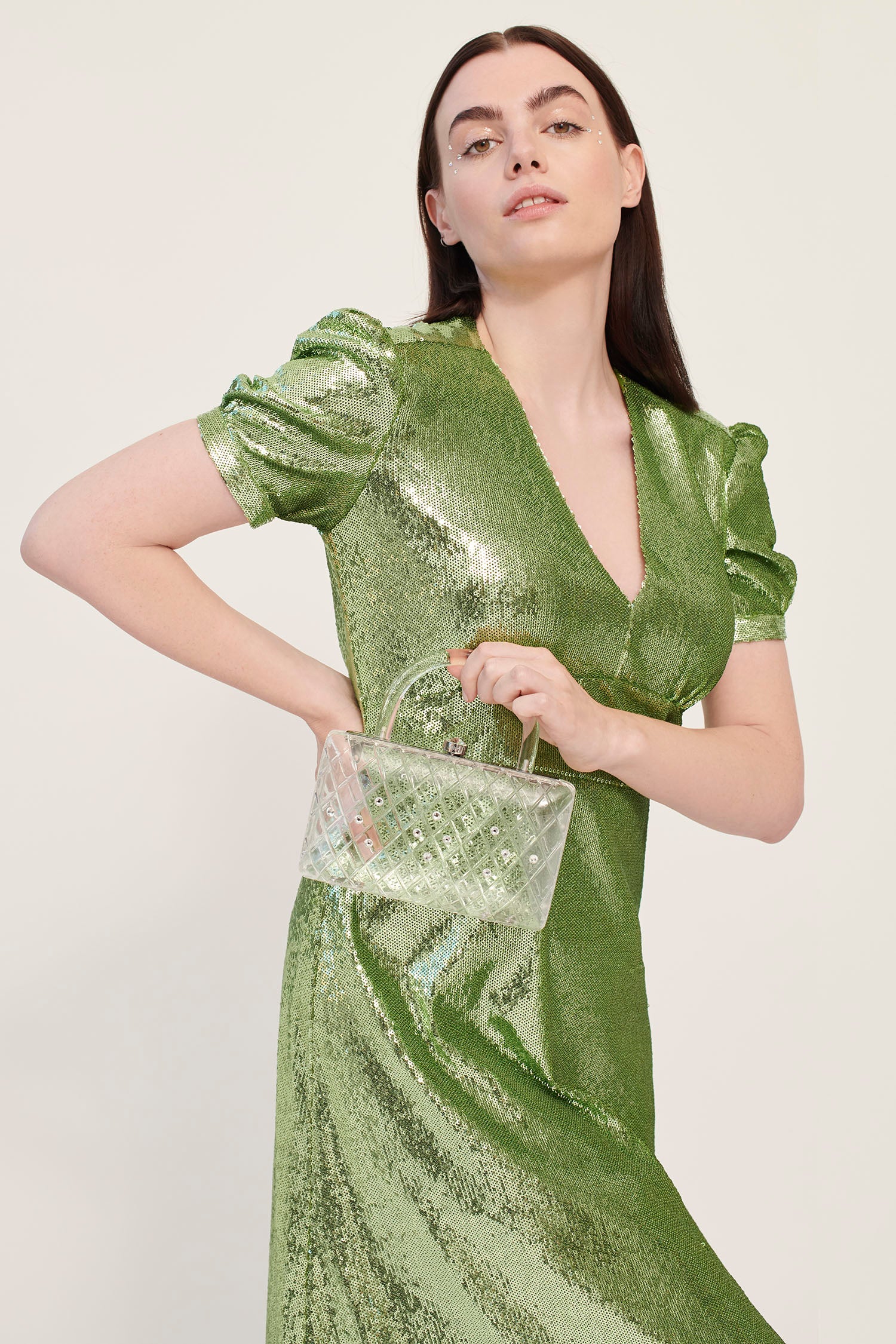 A model in a green dress holds a clear acrylic handbag with crystals and a short handle. 